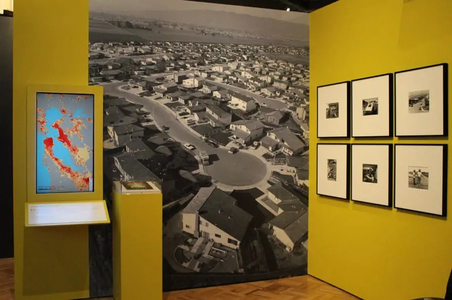 A photograph from Bill Owens' Suburbia series illustrates the changes brought by the new Bay Bridge when it was completed in the 1930s; a digital map showing the change in population density throughout the Bay Area further illuminates how the ease of automobile travel enabled development. Image courtesy of Oakland Museum of California.