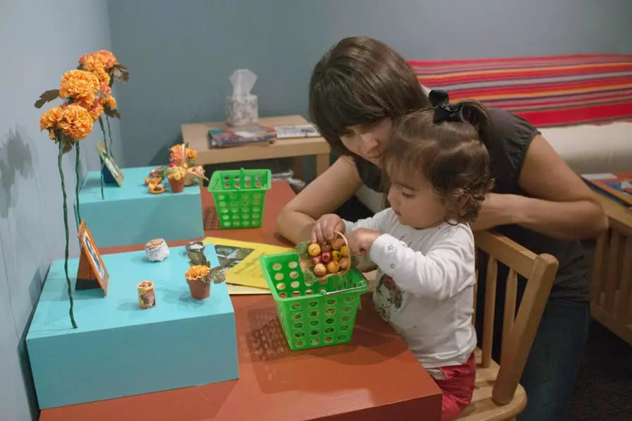 A mother and her child put together a miniature altar, one of several interactive elements in the exhibition The Tree of Life and Death: Días de los Muertos 2013, on view in the Gallery of California Natural Sciences at the Oakland Museum of California. Photo: Ace Lehner.