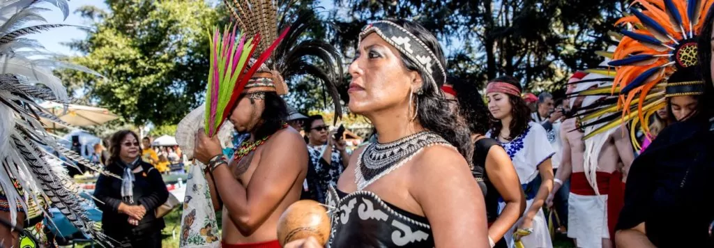 Aztec dancer in black with other dancers with headdresses at OMCA