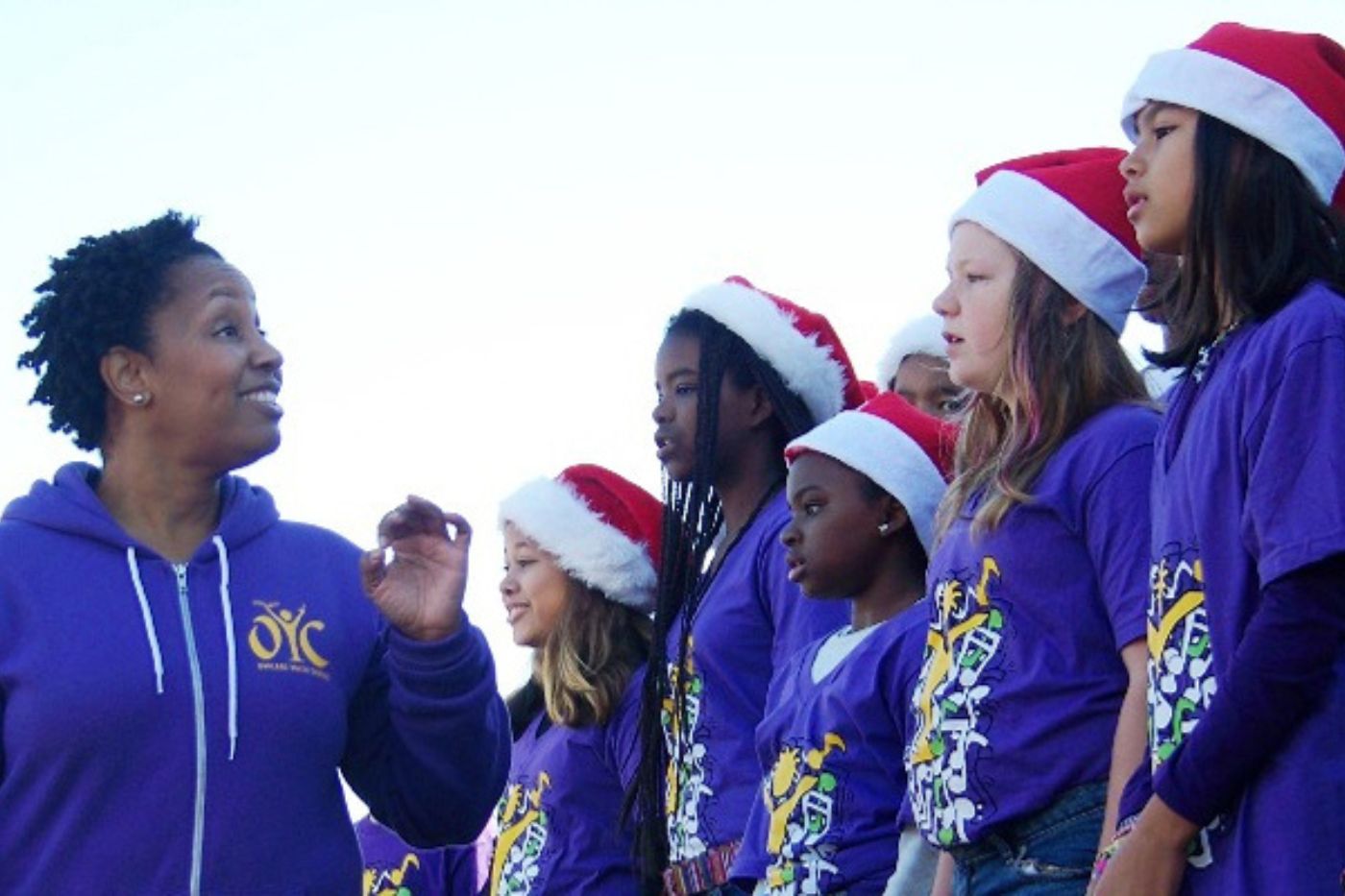 Oakland Youth singing in santa hats and purple shirts