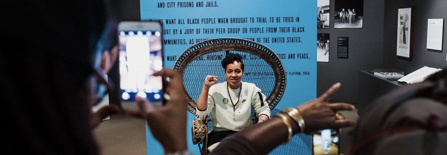 Person sitting in a chair holding up their fist while people take photos of them