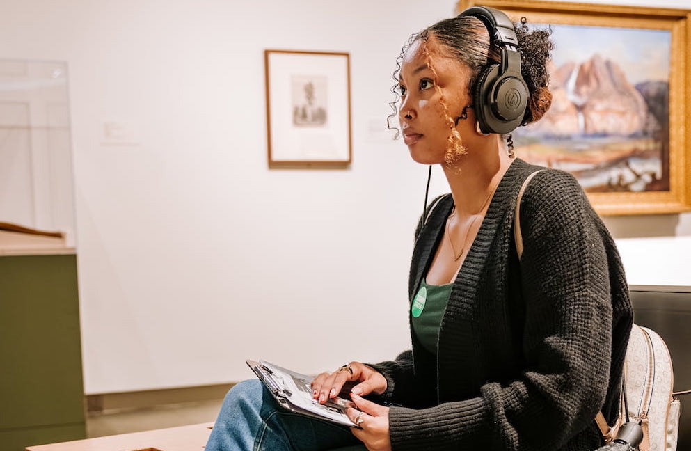 Museum visitor sitting down with headphones in gallery