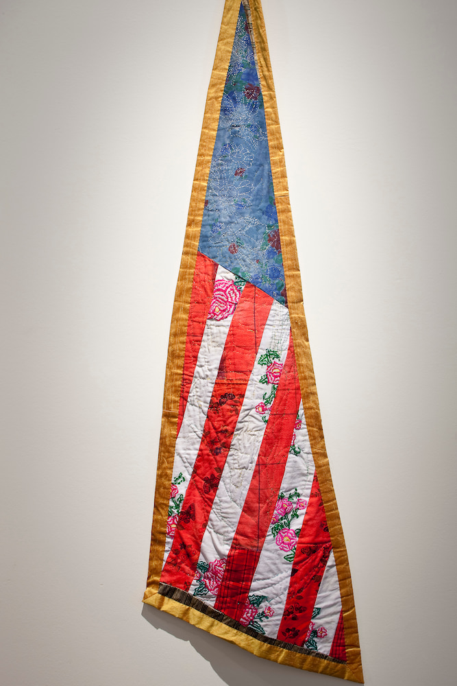 Image of art: A narrow triangular American flag, with flowers embroidered